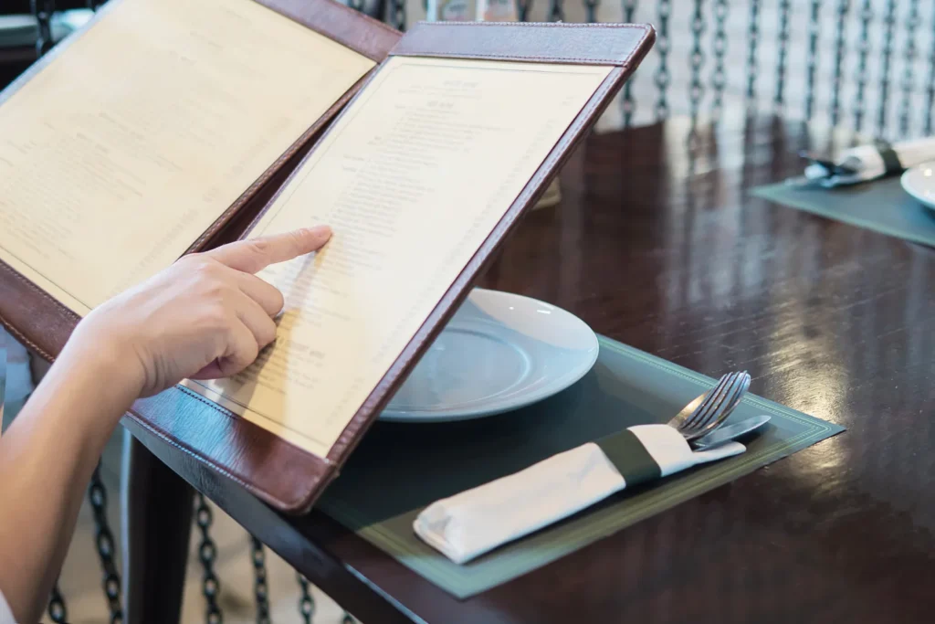 Cliente al tavolo di un ristorante che indica una voce del menu cartaceo