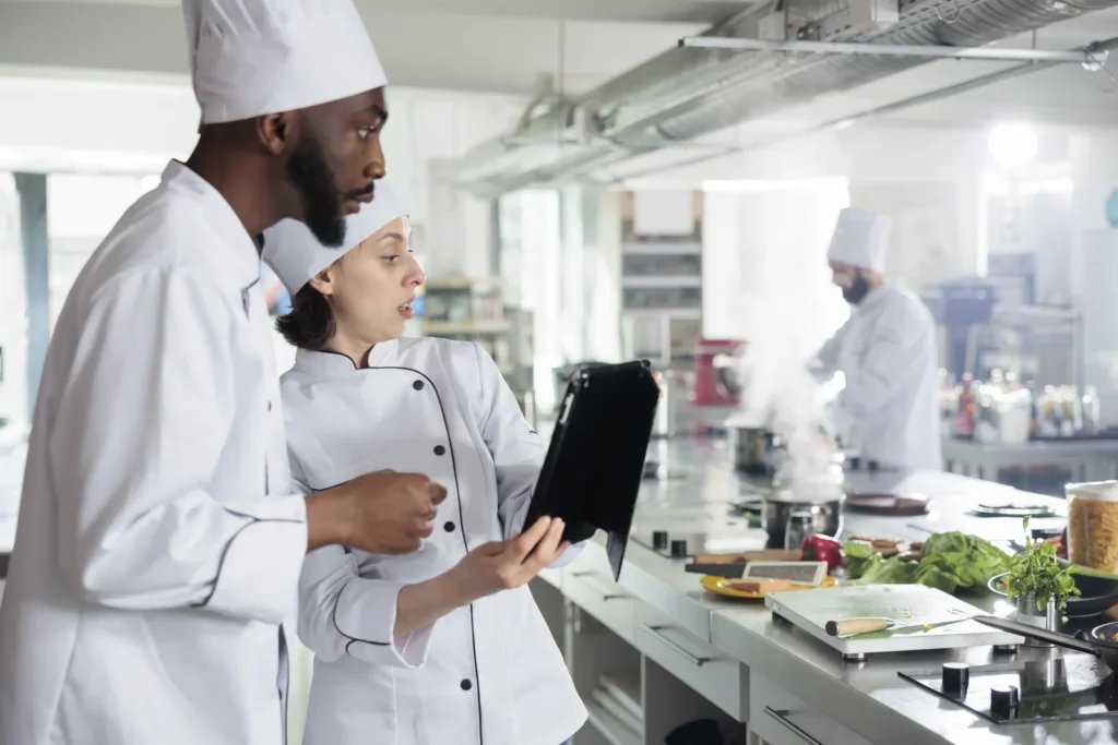 Due cuochi in divisa consultano un tablet in una cucina professionale