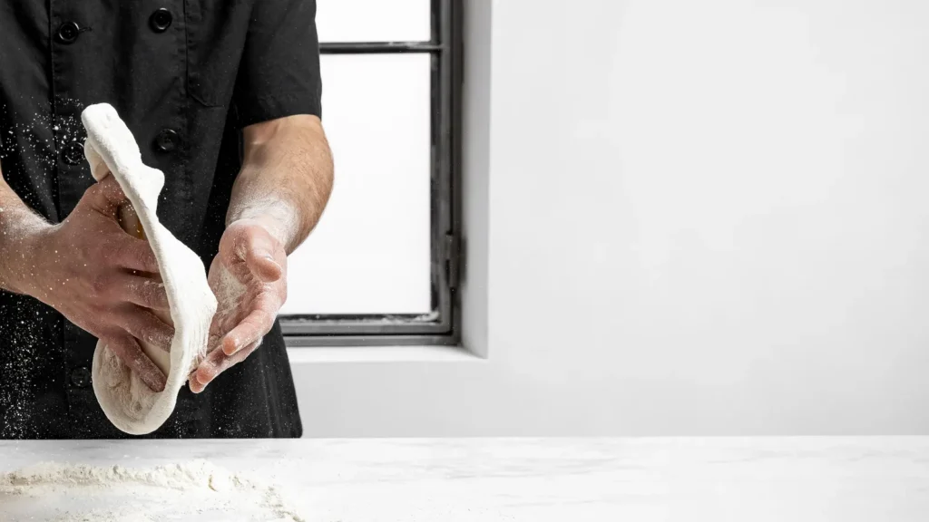 Pizzaiolo che allarga un panetto di impasto sul banco infarinato