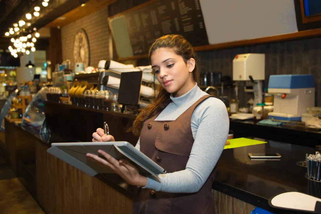 Titolare di un bar ristorante che aggiorna un registro al bancone del locale